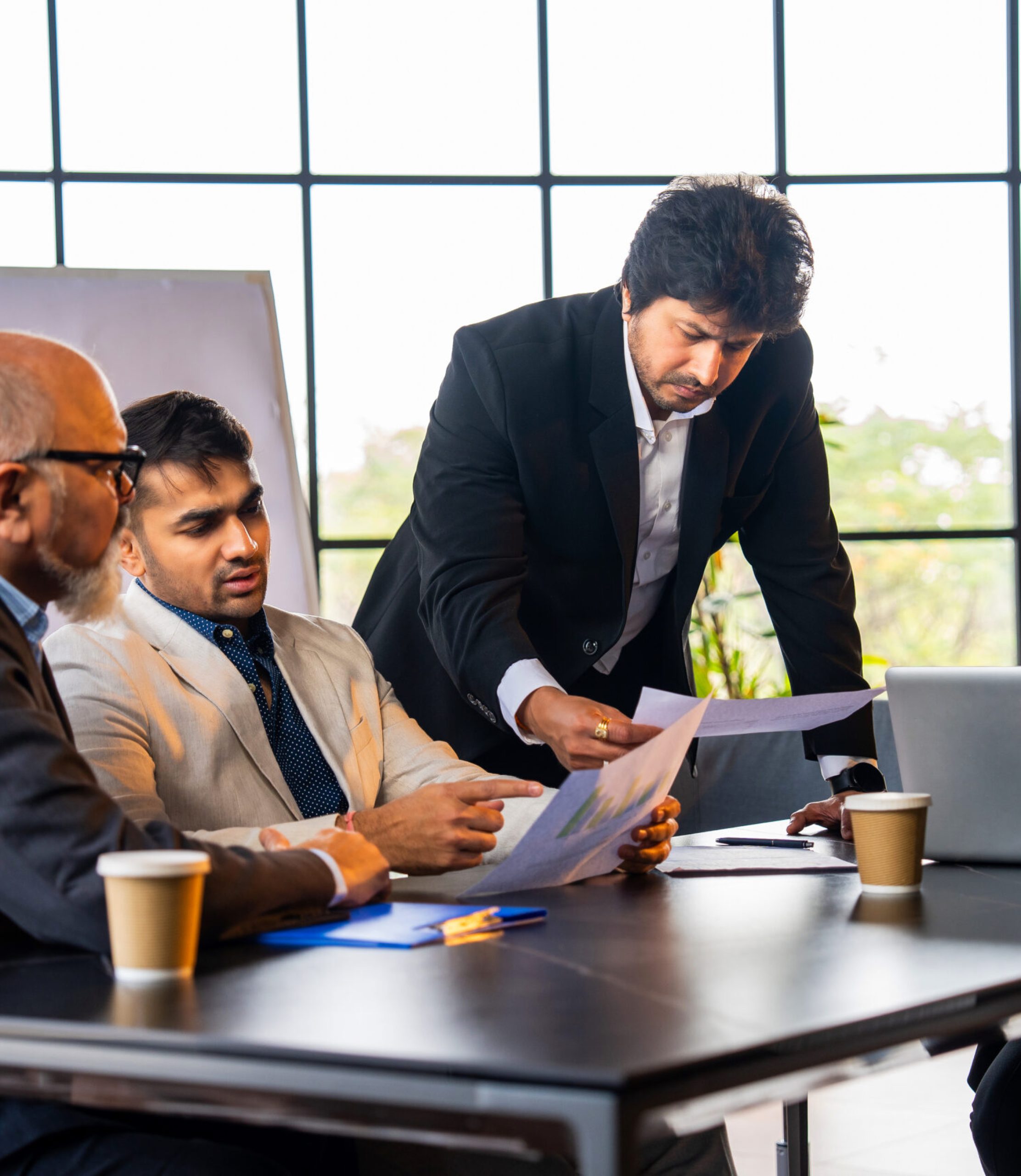 Indian Asian group of successful corporate professionals in formal attire working on laptop, reviewing business documents or reports, and discussing serious matters in an office setting